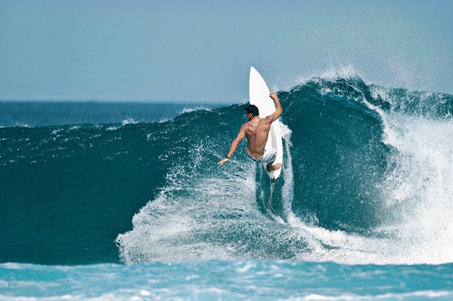 A surfer driving through a clean, turquoise wave